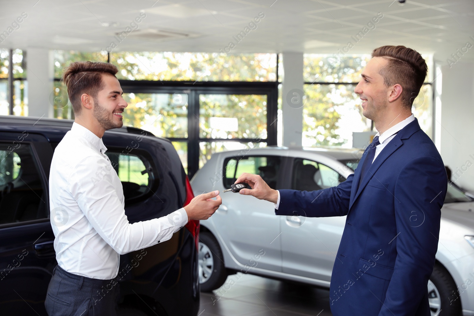Photo of Young salesman giving car key to client in dealership