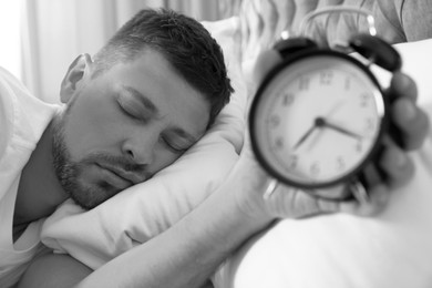 Image of Man with alarm clock sleeping at home in morning, selective focus. Black and white photography