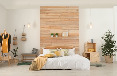 Stylish room interior with comfortable bed near wooden wall