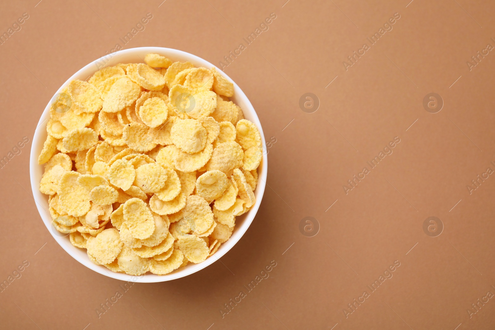 Photo of Breakfast cereal. Tasty corn flakes in bowl on brown table, top view. Space for text