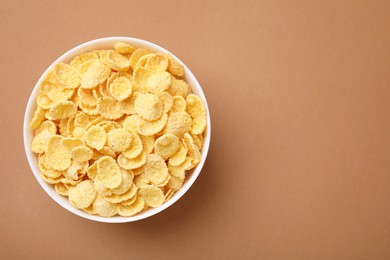 Photo of Breakfast cereal. Tasty corn flakes in bowl on brown table, top view. Space for text