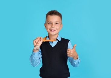 Photo of Happy boy in school uniform with golden medal on blue background