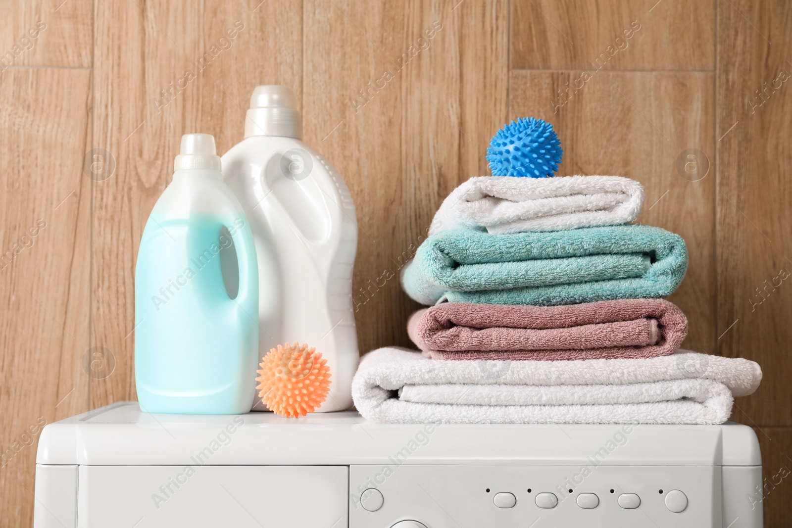 Photo of Dryer balls, stacked clean towels and detergents on washing machine