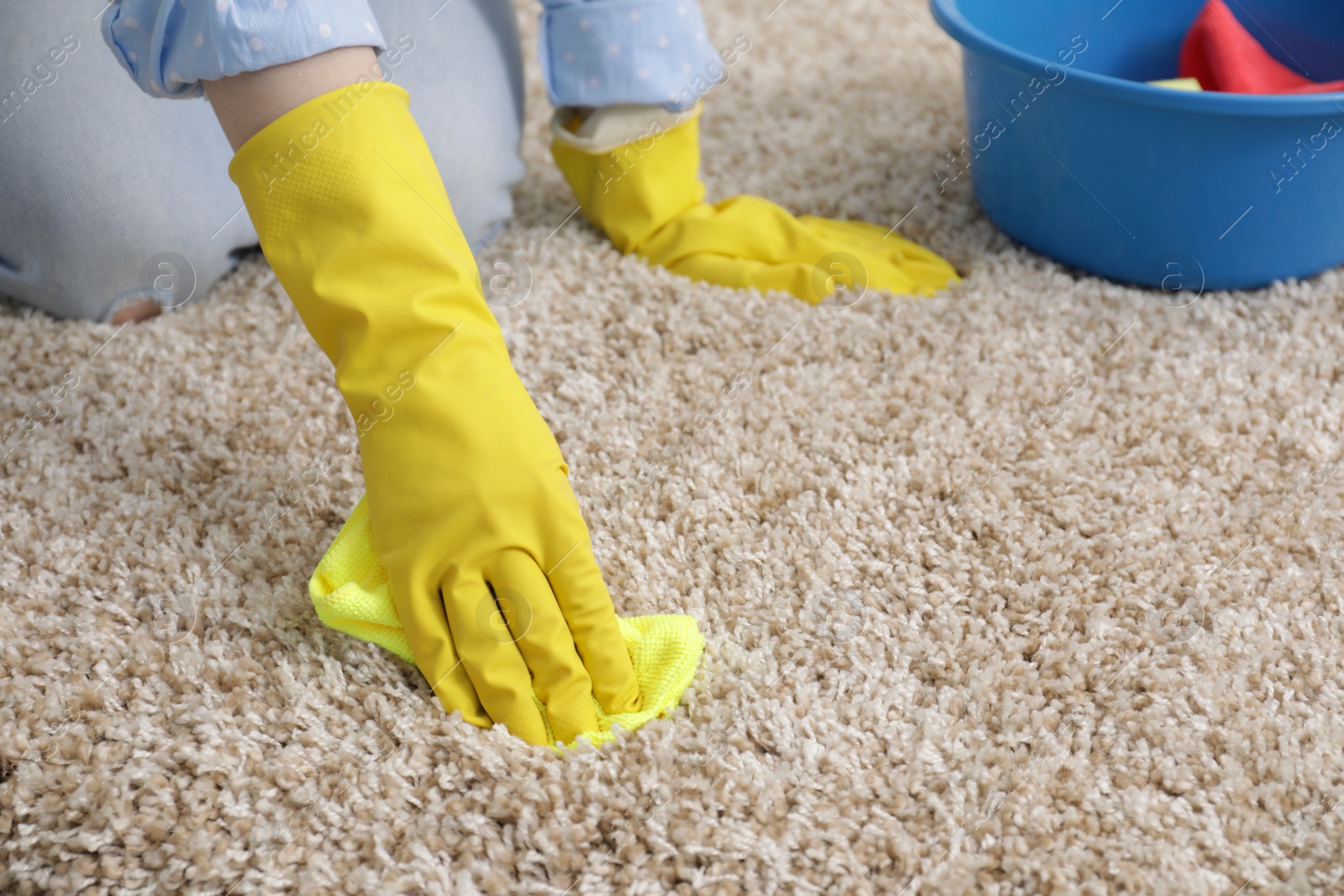 Photo of Woman in rubber gloves cleaning carpet with rag, closeup