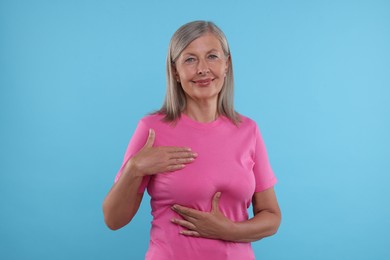 Beautiful senior woman doing breast self-examination on light blue background