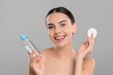 Beautiful woman holding makeup remover and cotton pad on light grey background