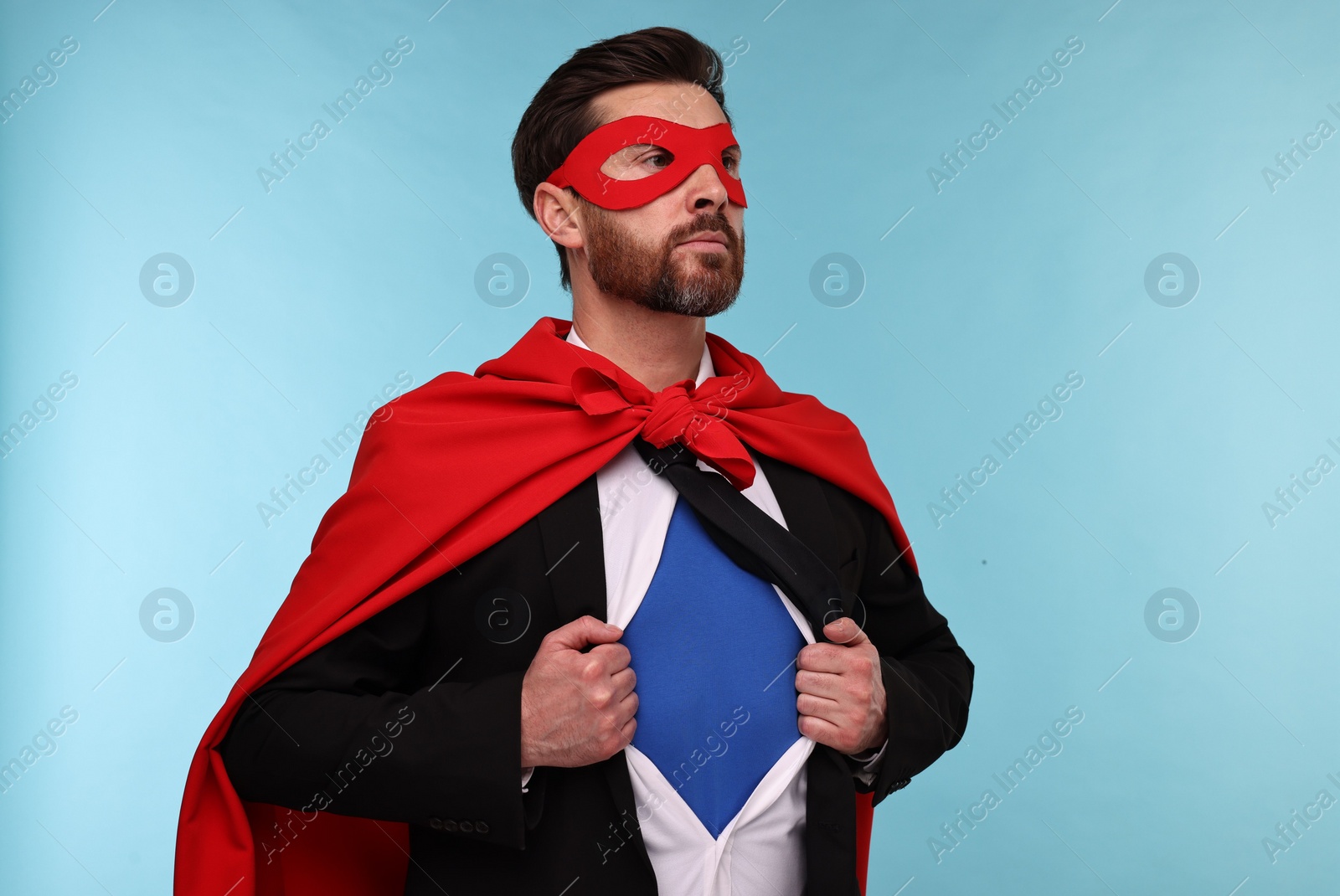 Photo of Confident businessman wearing superhero costume under suit on light blue background