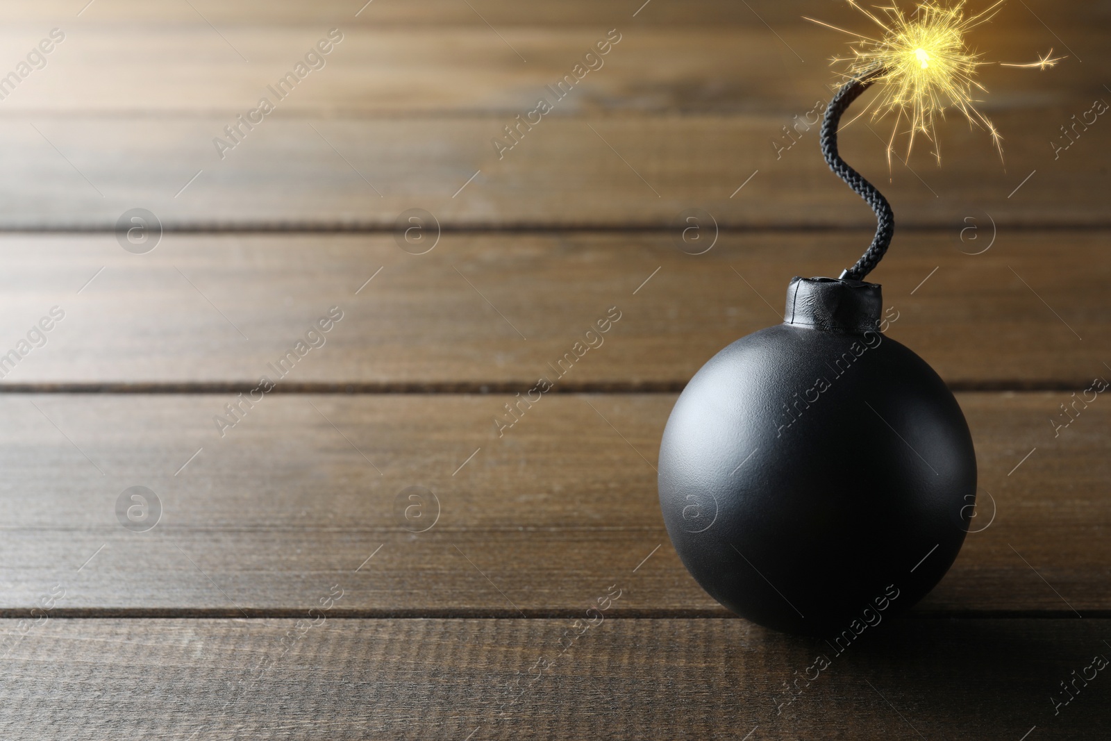 Image of Old fashioned black bomb with lit fuse on wooden table, space for text