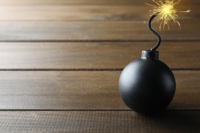 Old fashioned black bomb with lit fuse on wooden table, space for text