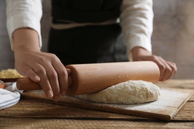 Woman rolling raw dough at wooden table, closeup