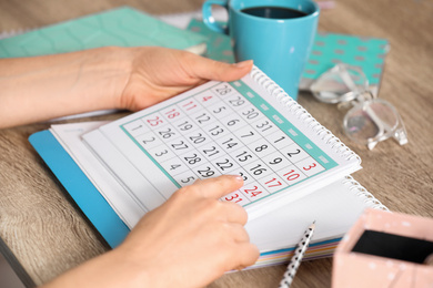 Photo of Woman with calendar at wooden table, closeup