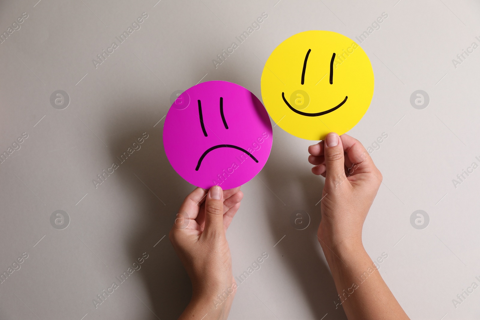 Photo of Choice concept. Woman holding papers with sad and happy emoticons on light grey background, closeup