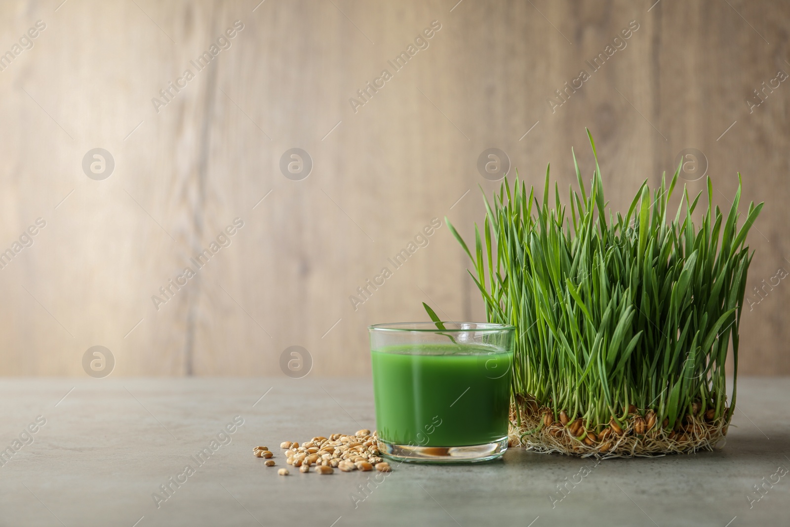 Photo of Glass of juice, sprouted wheat grass and grains on table. Space for text