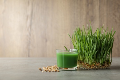 Photo of Glass of juice, sprouted wheat grass and grains on table. Space for text