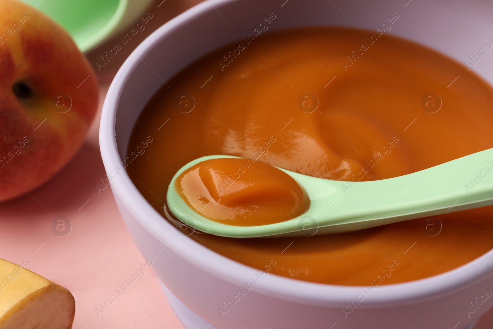 Photo of Healthy baby food in bowl on pink table, closeup