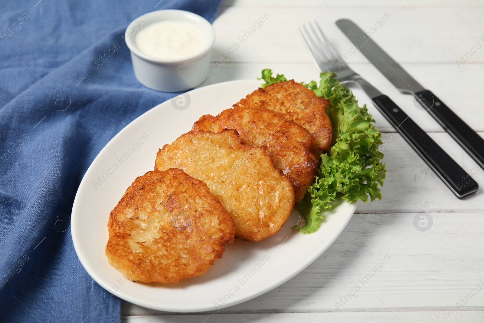 Photo of Plate with tasty potato fritters and sauce on wooden table