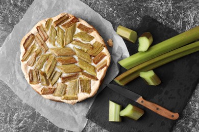 Photo of Freshly baked rhubarb pie, stalks and knife on grey textured table, flat lay