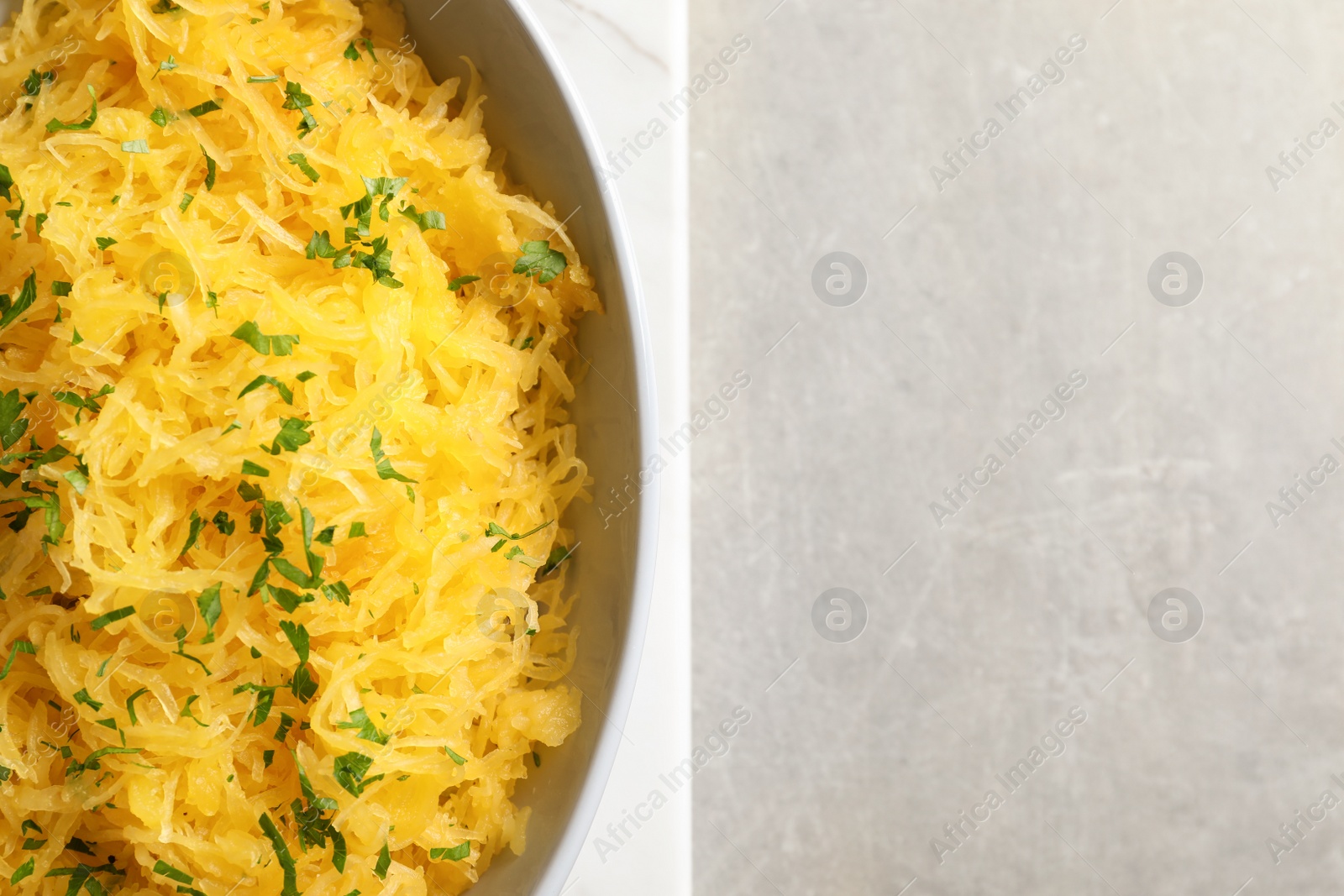 Photo of Bowl with cooked spaghetti squash on light background, top view. Space for text