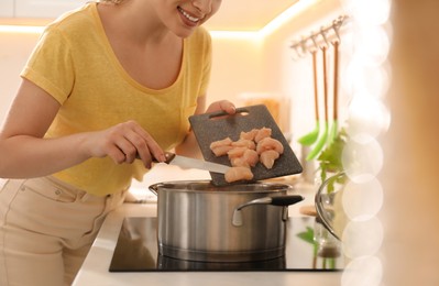 Photo of Woman putting meat into pot to make bouillon in kitchen, closeup. Homemade recipe