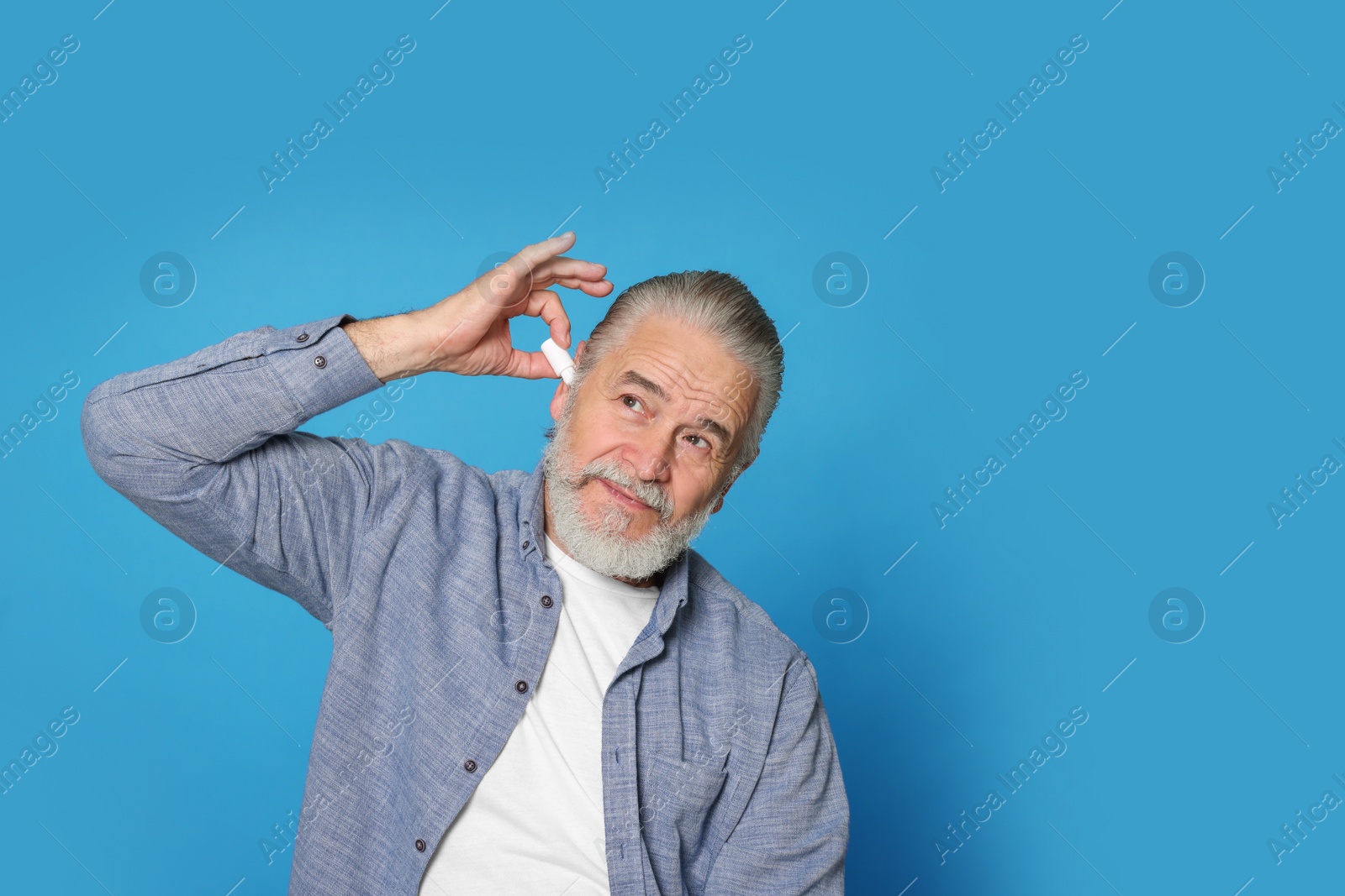 Photo of Senior man using ear drops on light blue background, space for text