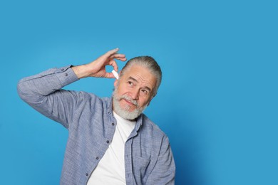 Senior man using ear drops on light blue background, space for text
