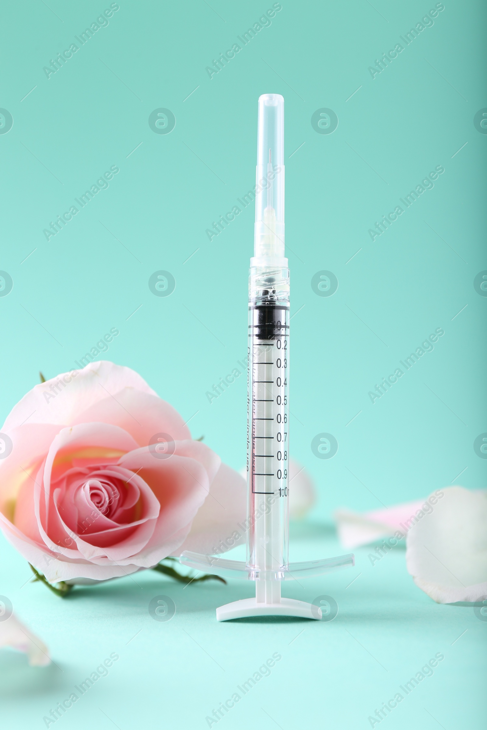 Photo of Cosmetology. Medical syringe, rose flower and petals on turquoise background