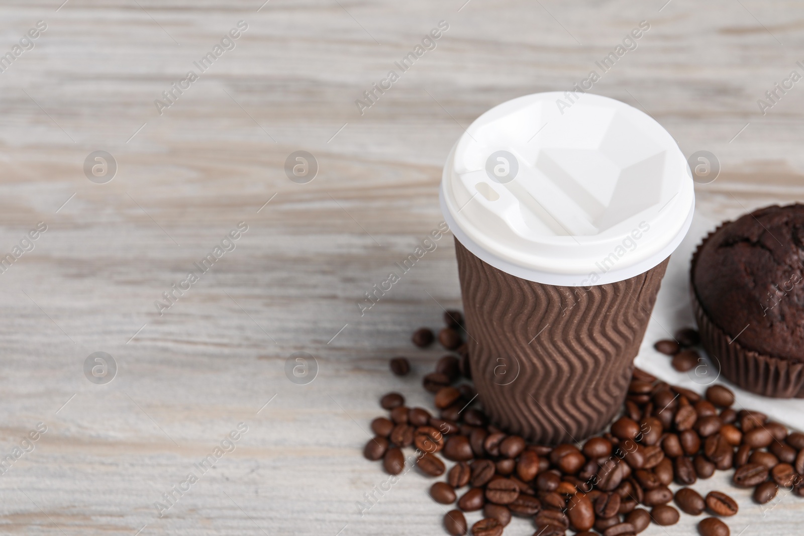 Photo of Paper cup, coffee beans and muffin on wooden table, space for text. Coffee to go