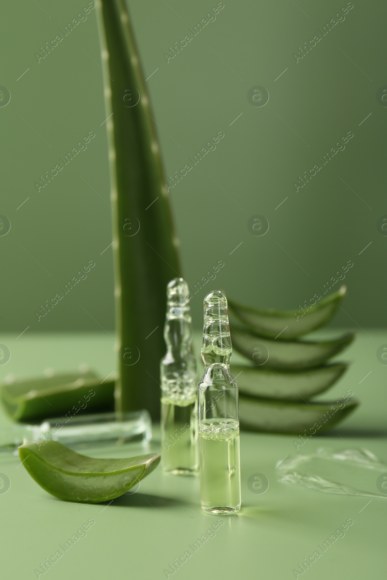 Photo of Skincare ampoules with extract of aloe vera and cut green leaves on color background