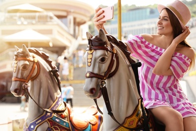 Photo of Young pretty woman taking selfie on carousel in amusement park