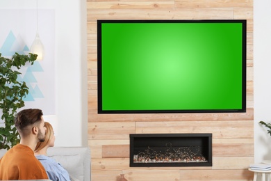 Photo of Couple watching TV on sofa in living room with decorative fireplace