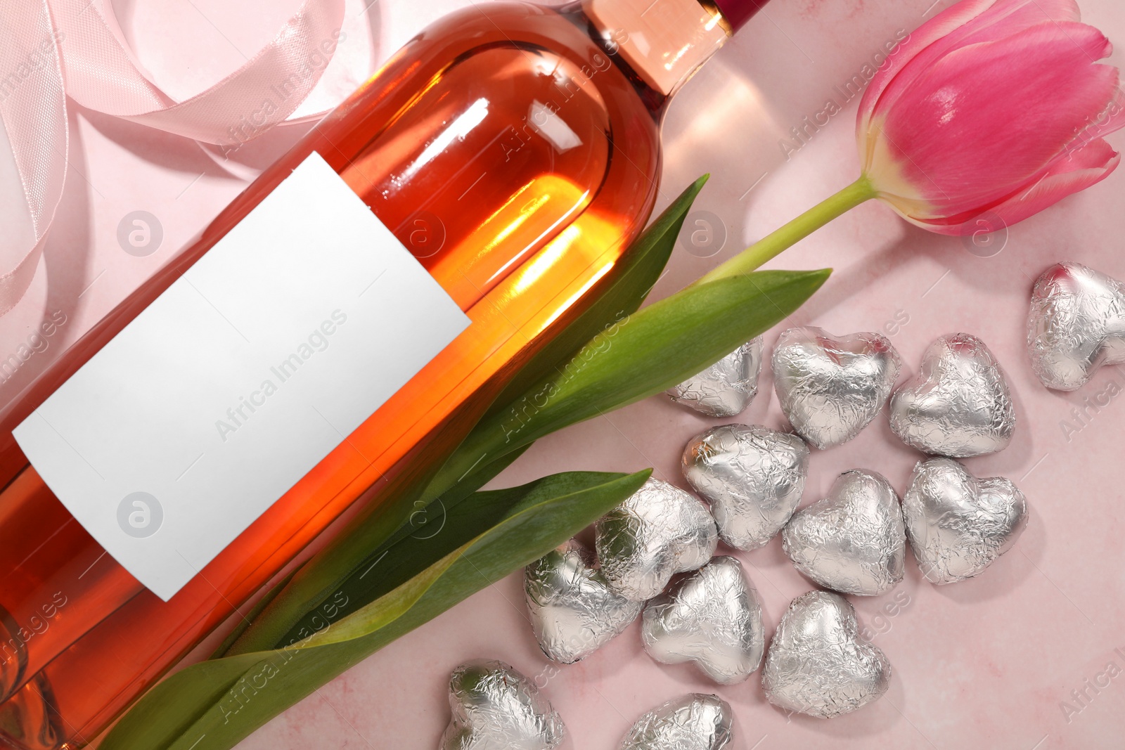 Photo of Delicious heart shaped chocolate candies, beautiful tulip and bottle of wine on pink table, flat lay