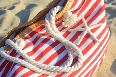 Stylish striped bag with dry starfish on sandy beach, closeup