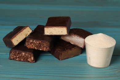 Pieces of tasty bars and cup with protein powder on light blue wooden table