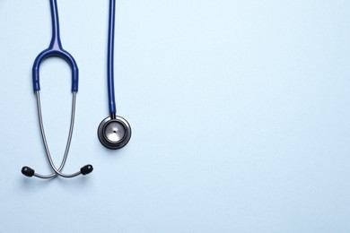 Stethoscope on light blue background, top view. Space for text