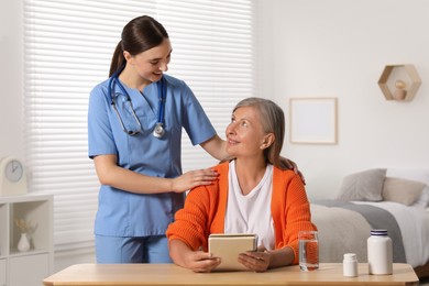 Young healthcare worker consulting senior woman at wooden table indoors