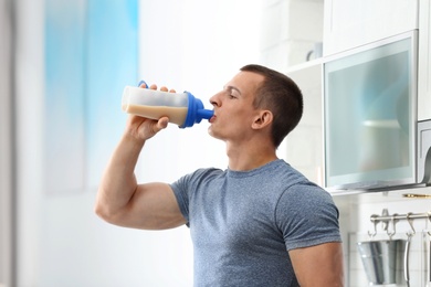 Athletic young man drinking protein shake in kitchen