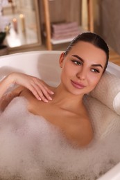 Young woman using pillow while enjoying bubble bath indoors