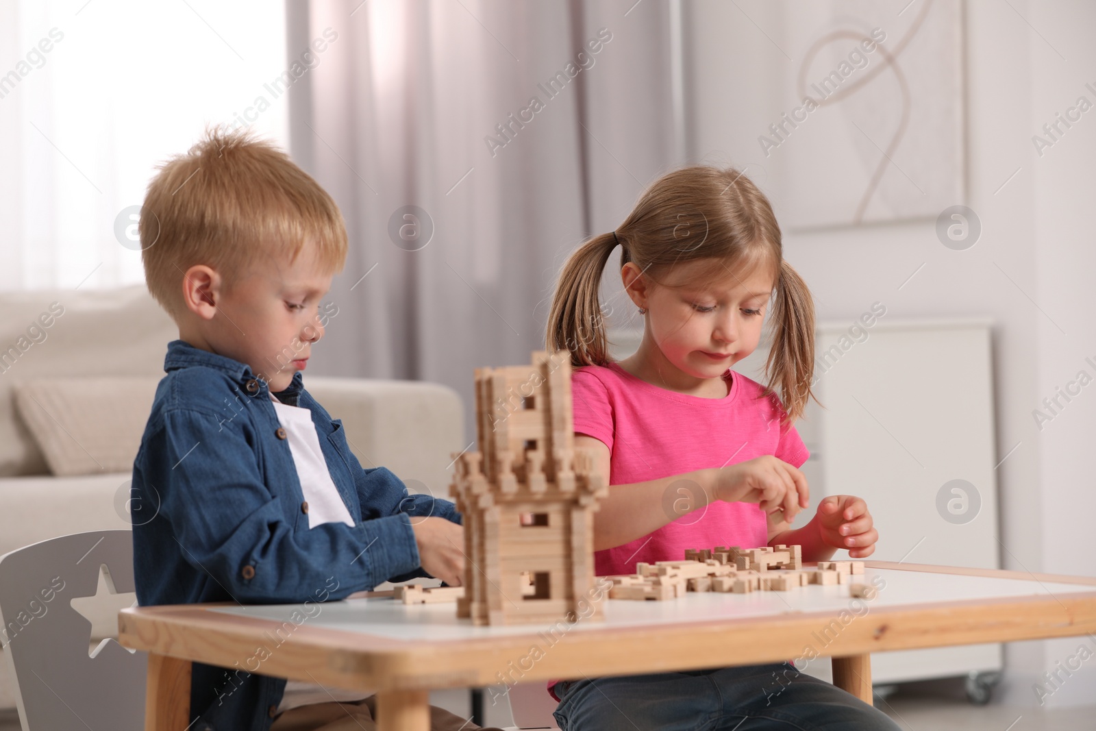 Photo of Little girl and boy playing with wooden tower at table indoors. Children's toy