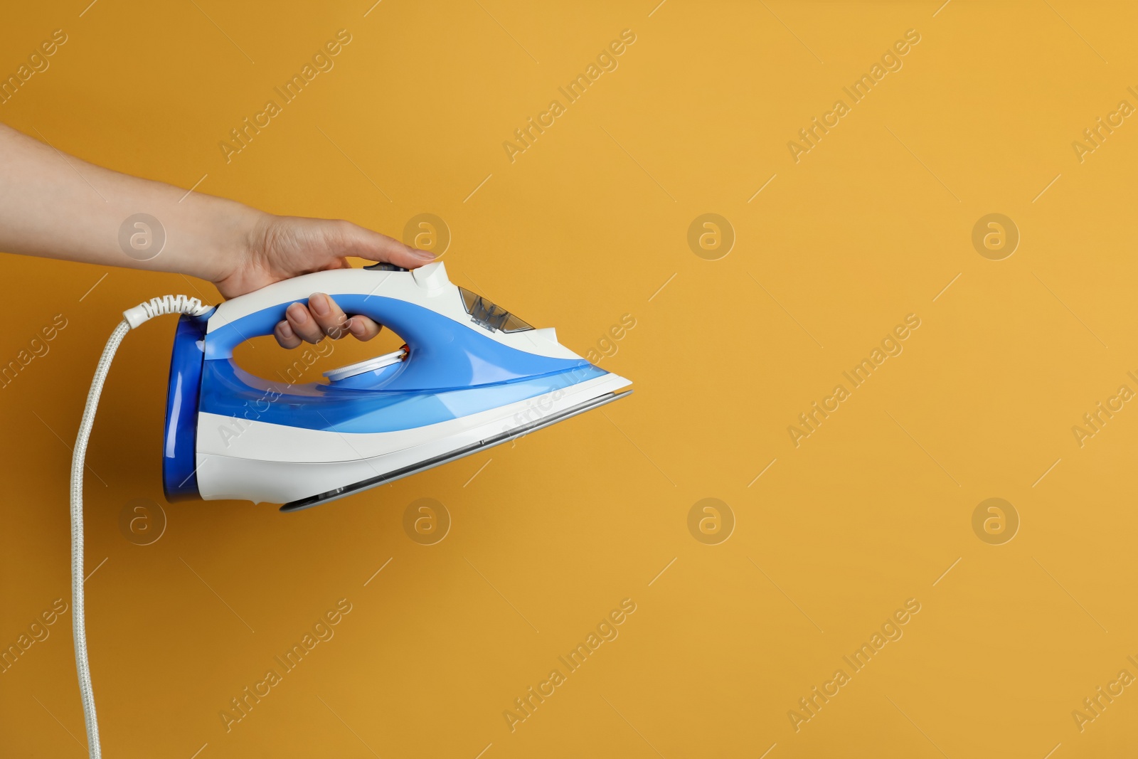 Photo of Woman holding modern iron on orange background, closeup. Space for text