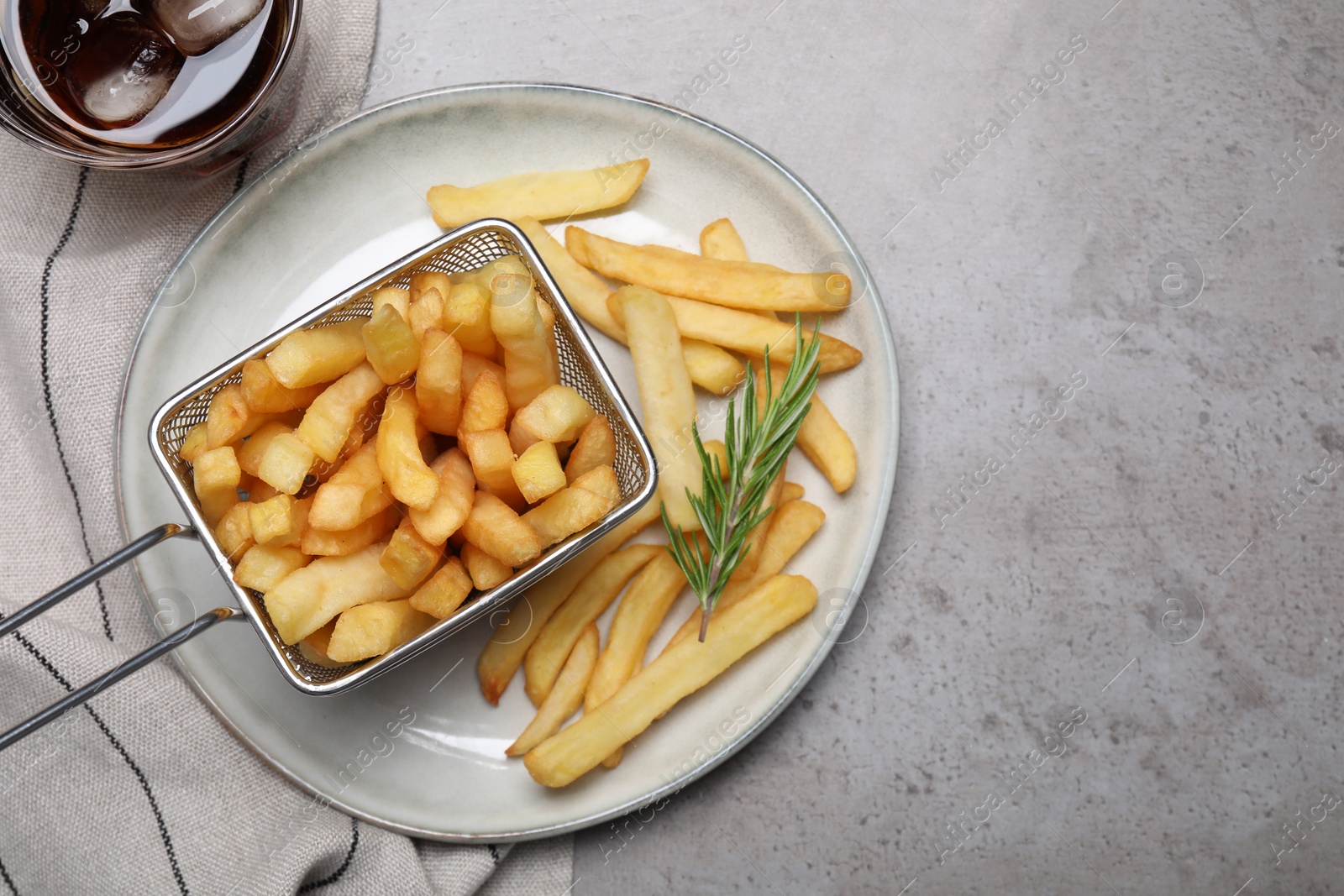 Photo of Tasty french fries with rosemary and soda drink on light grey table, flat lay. Space for text