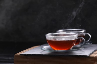 Photo of Aromatic hot tea in glass cups on table against black background. Space for text