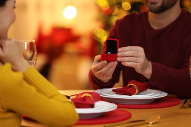 Photo of Man with engagement ring making proposal to his girlfriend at home on Christmas, closeup