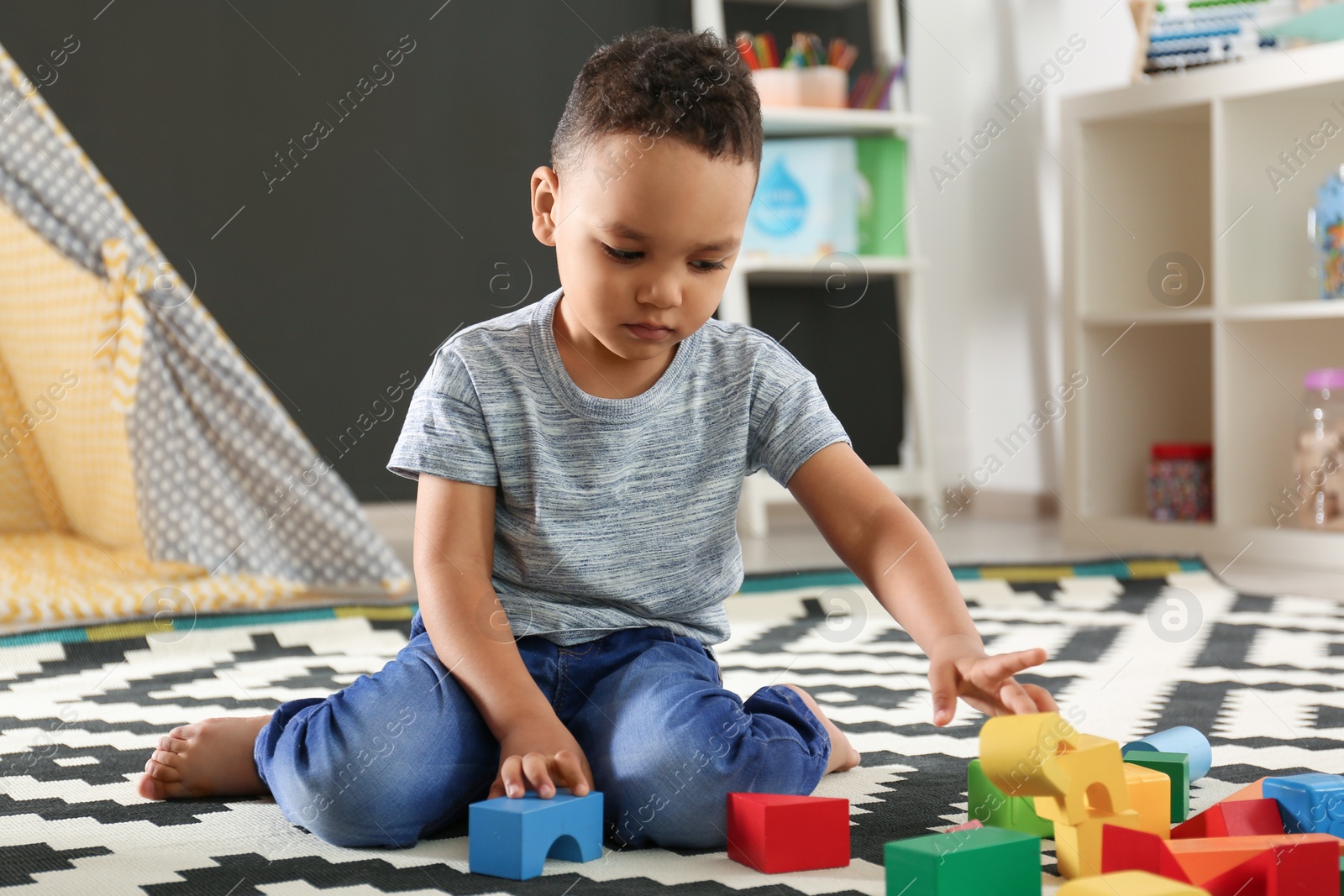 Photo of Cute little African-American child playing with building blocks on floor in kindergarten. Indoor activity