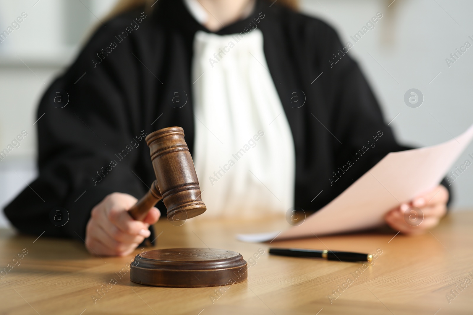 Photo of Judge striking mallet at wooden table in courtroom, closeup