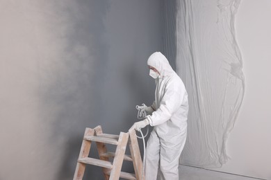 Photo of Decorator with spray paint near ladder and walls indoors