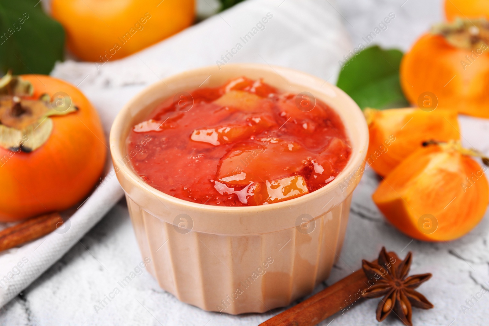 Photo of Bowl of tasty persimmon jam and ingredients on white textured table