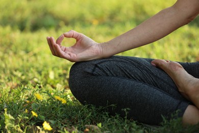 Woman meditating on green grass, closeup view