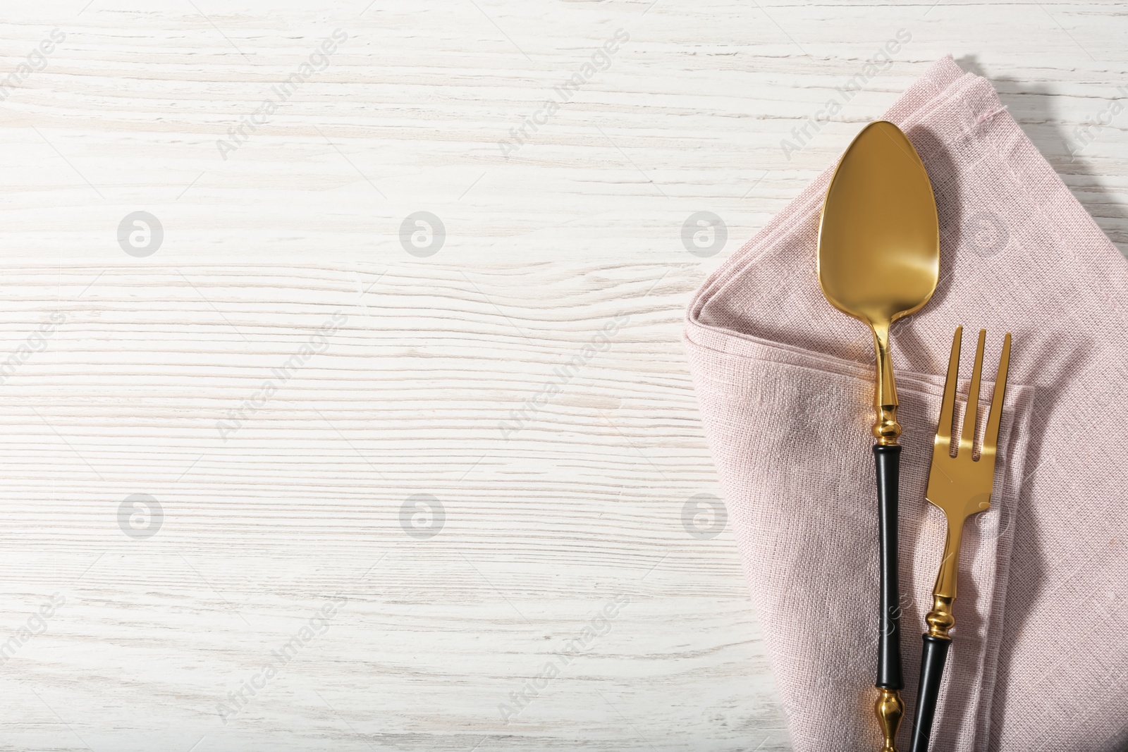 Photo of Shiny fork, spoon and napkin on white wooden table, top view. Space for text