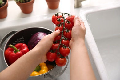 Woman washing fresh cherry tomatoes in kitchen sink, closeup