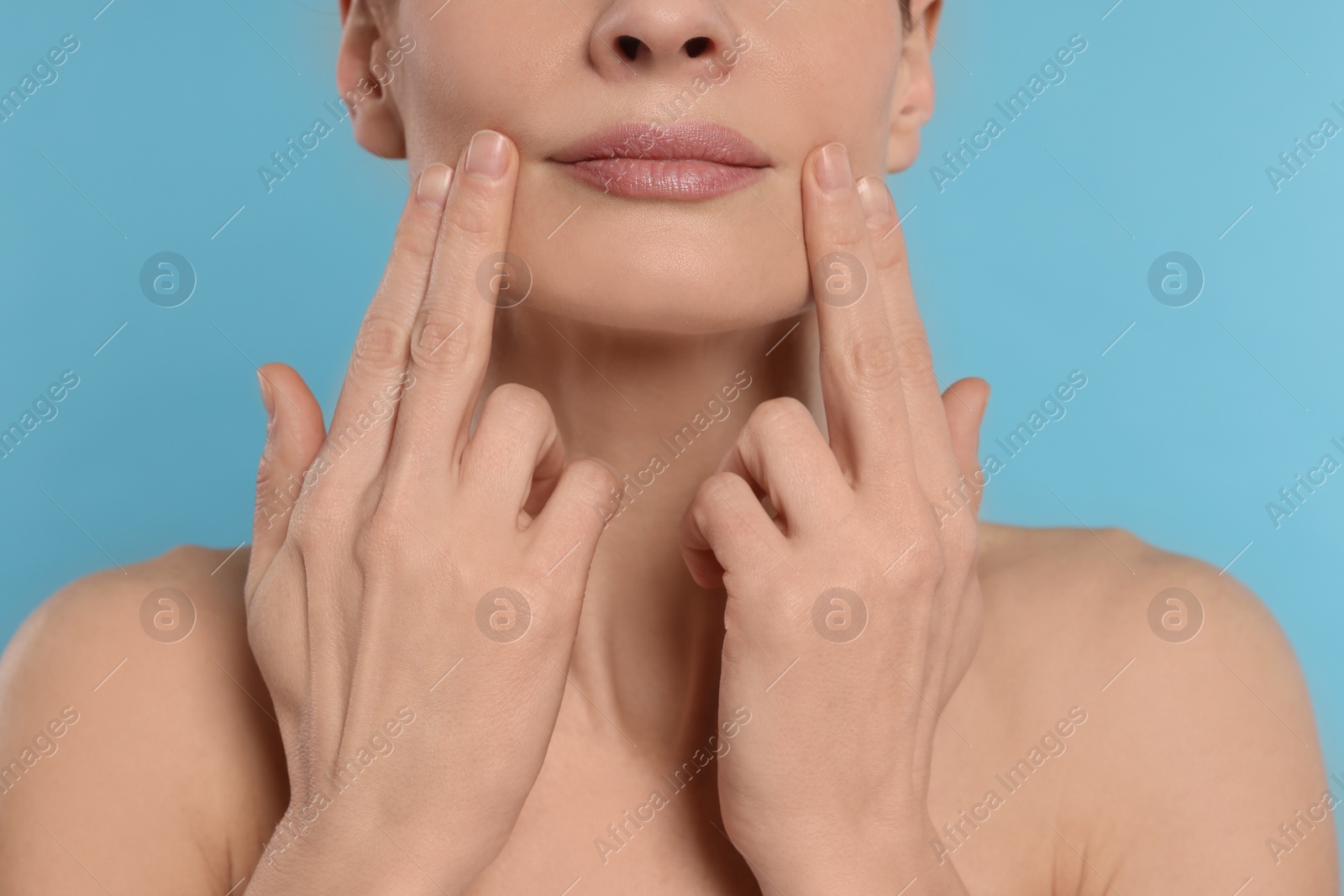 Photo of Woman massaging her face on turquoise background, closeup